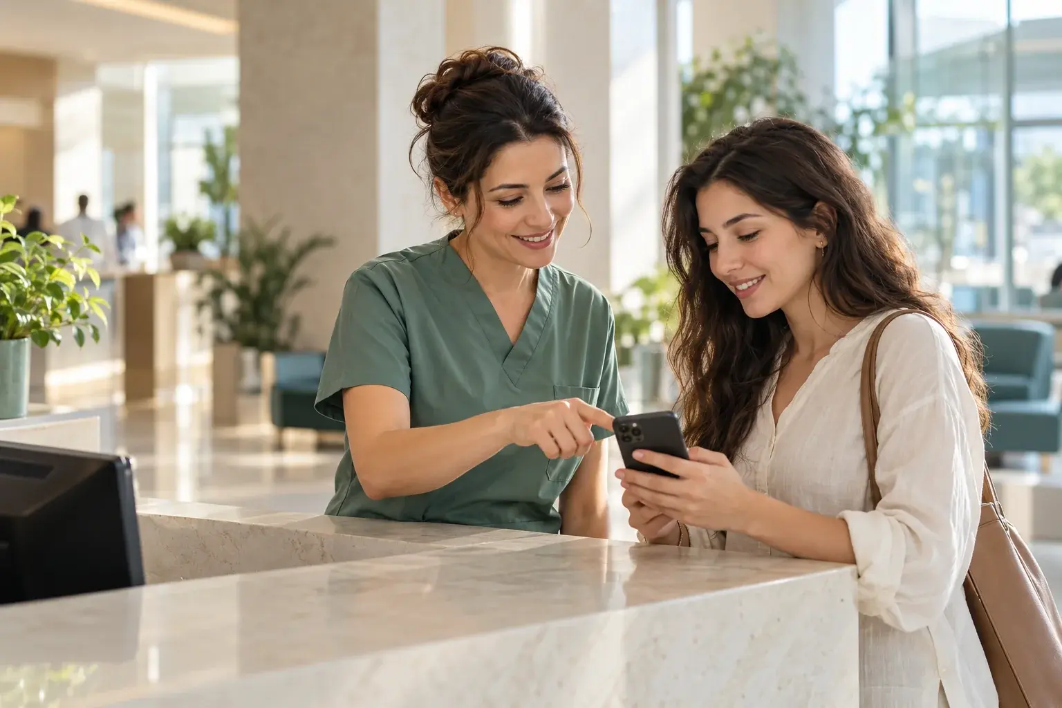 Hastane danışma alanında telefon kullanan bir ziyaretçiye yardımcı olan sağlık çalışanı